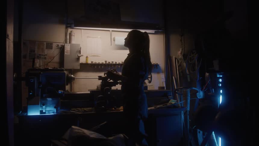 Woman in silhouette works at a lit bench inside the workshop