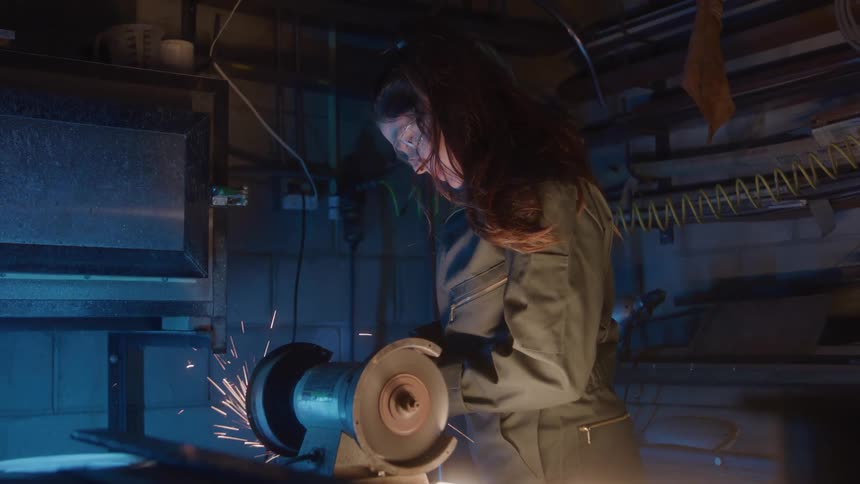 Woman wears safety glasses while working on a grinder releasing sparks