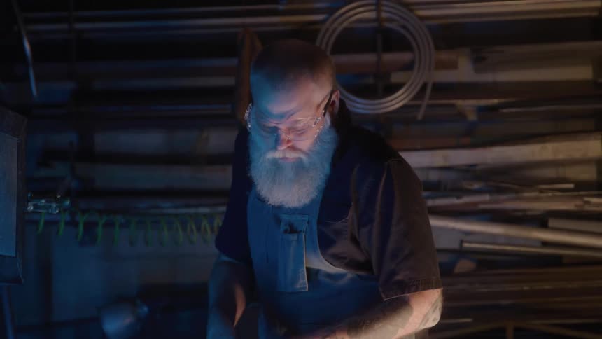 Man with a white beard wears safety glasses while working in the workshop