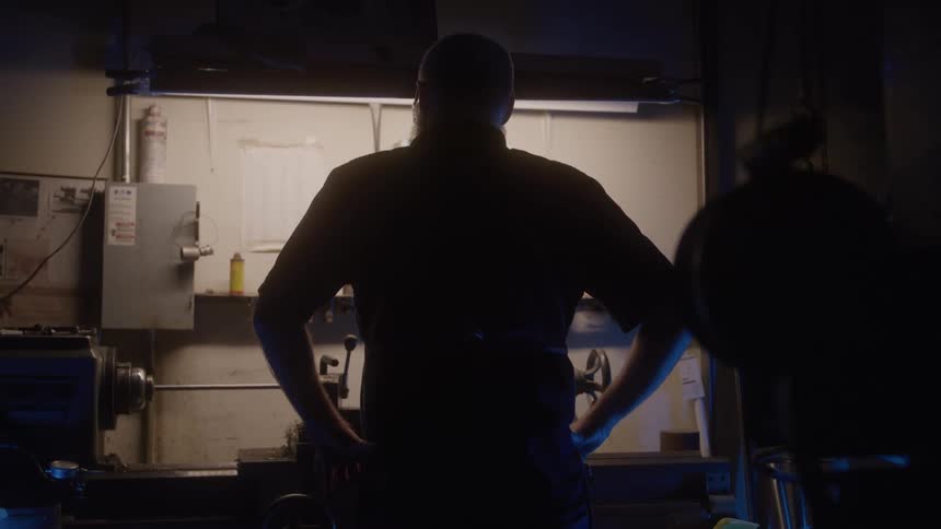 Man looks at a lit workbench in a workshop