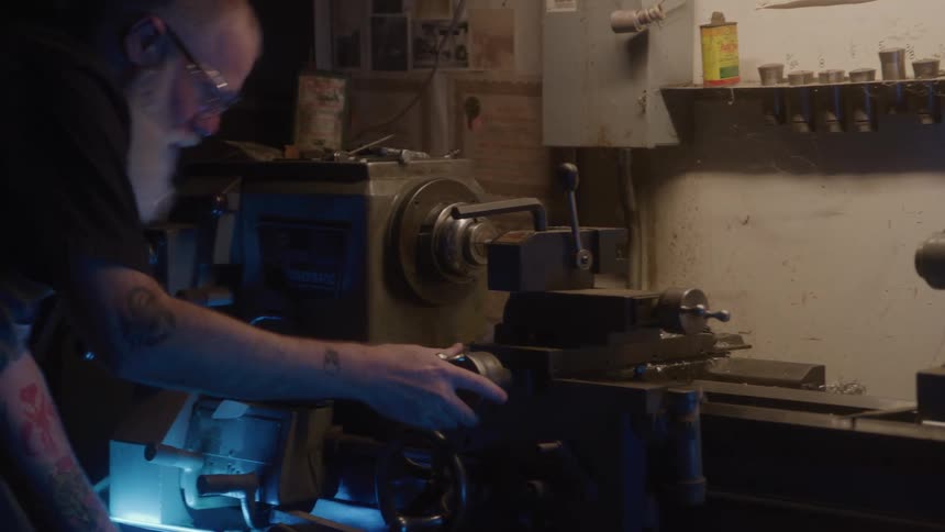 Man wearing safety glasses adjusts a piece on a lathe in the workshop