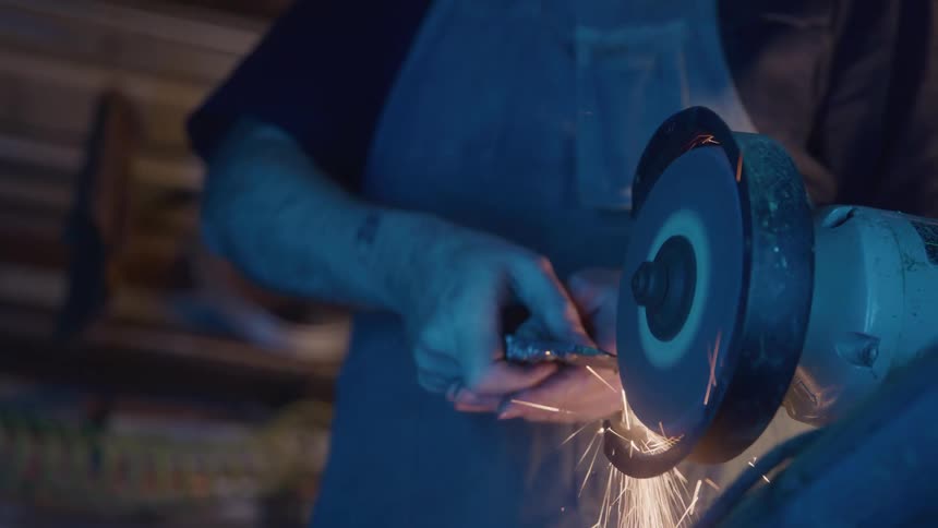 Closeup of hands grinding metal on a grinder with sparks