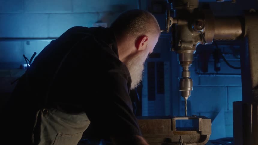 Man operates a drill press holding a piece in the workshop