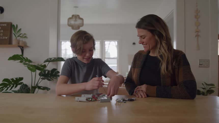 Boy assembles an electronic circuit while the mother watches with a smile