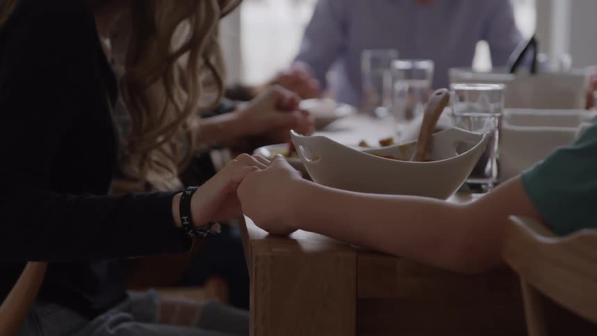 Hands held in prayer around the dining table before the meal