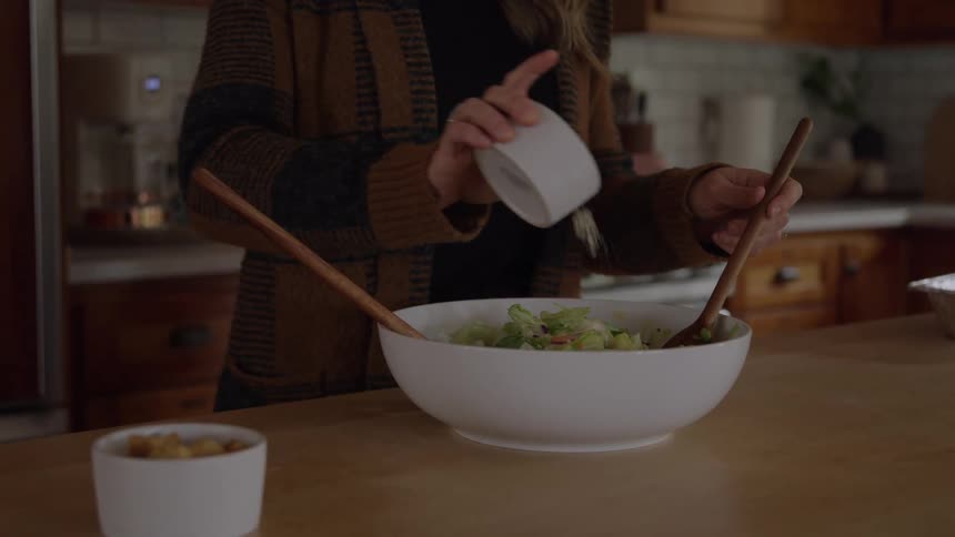 Woman prepares salad in a white bowl on the kitchen counter