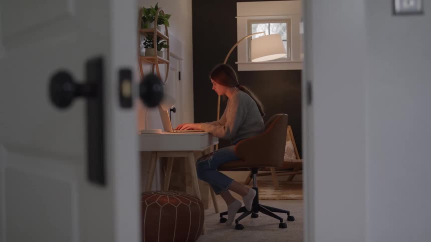 Young woman sitting at a desk works on the computer in a lit room