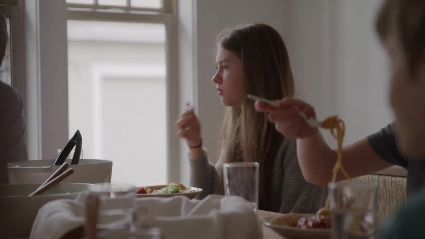 Teenage girl having supper with her family at the dining table engaged in conversation as they enjoy their meal together