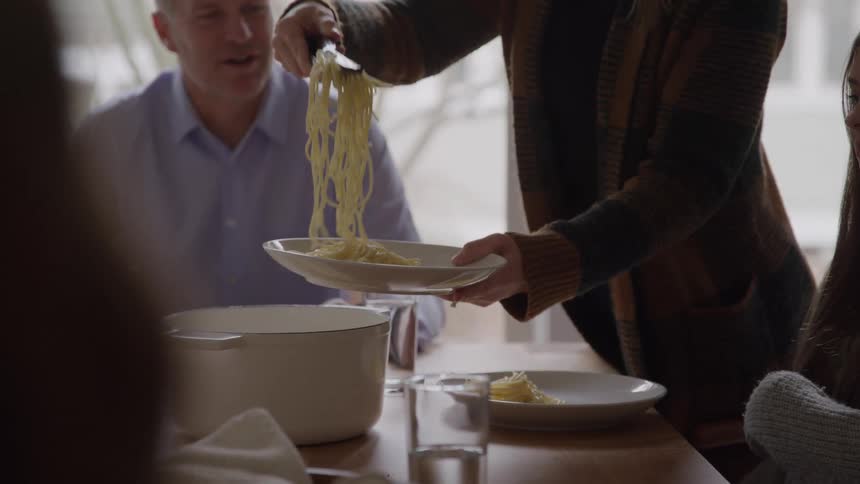 Woman serves pasta onto a plate during a family meal