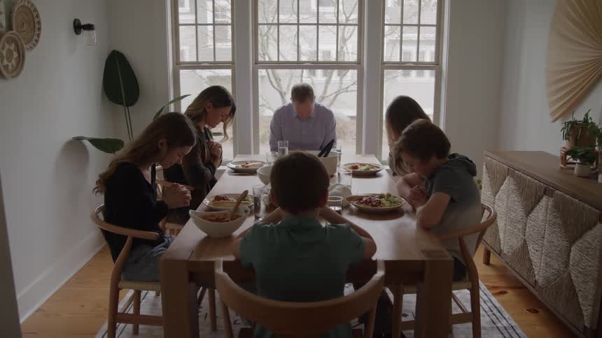 Family gathered at the table says a prayer before the meal