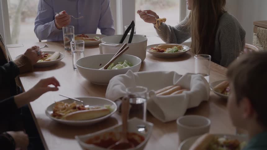 Family gathered at the table shares a meal with pasta salad and bread