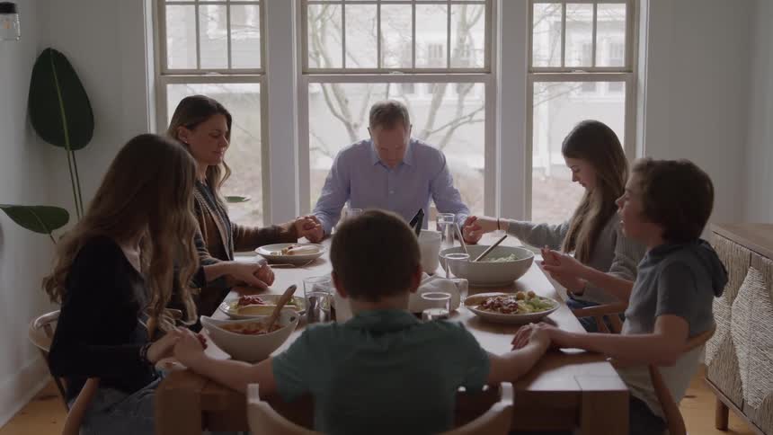 Family holding hands says a prayer before the meal at the dining table