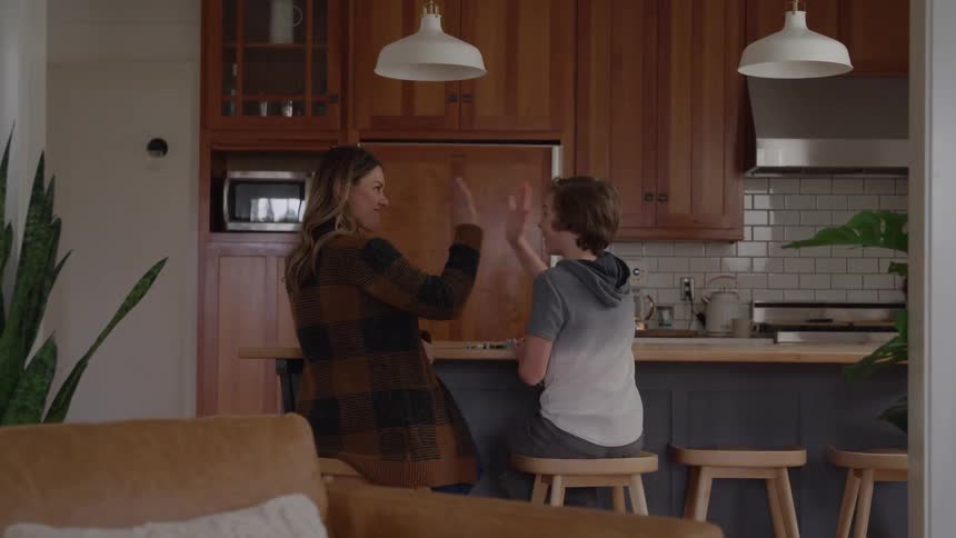 Mother and son playing a card game at the dining table with the mother giving her son a high five afterward in celebration