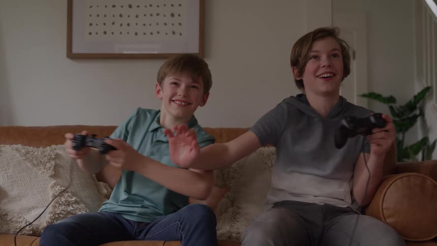Two brothers play video games smiling on the living room couch