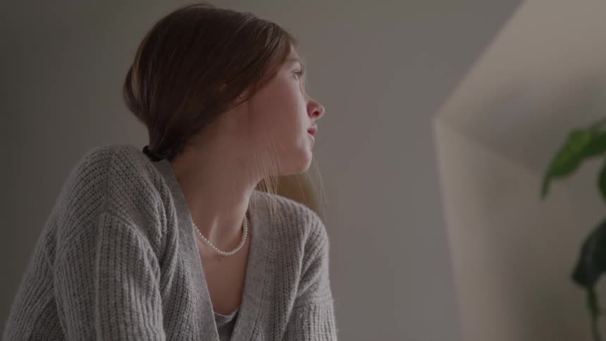 Young woman in a gray sweater looks thoughtfully to the side