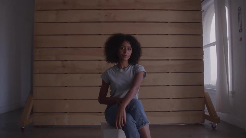 A woman sits on a chair posing against a wooden backdrop