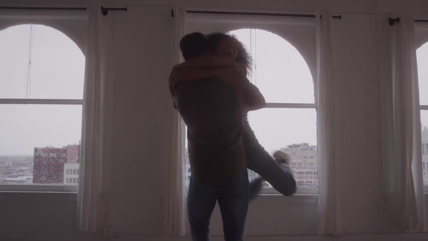 A couple joyfully embraces in an empty loft with tall arched windows