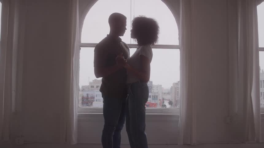 A couple are slow dancing by the window
