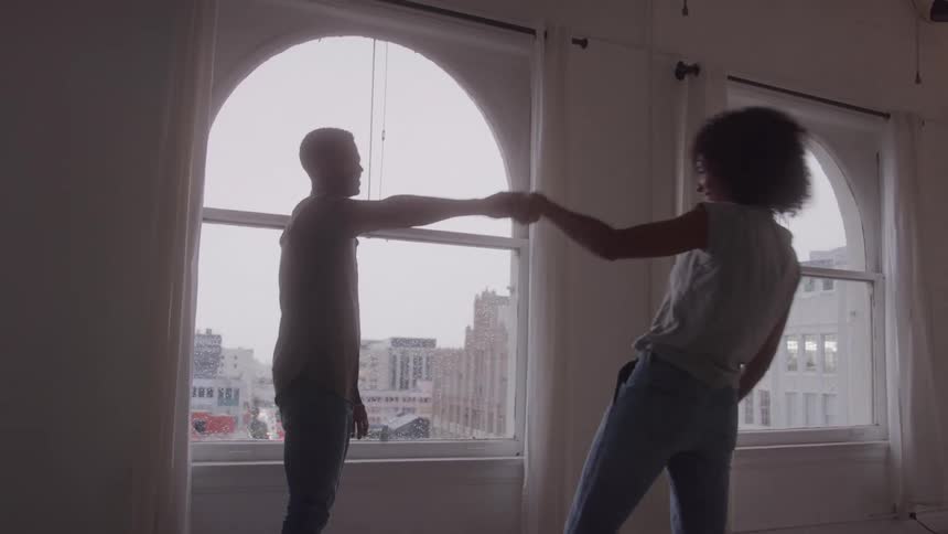 A couple shares an intimate kiss in front of large arched windows