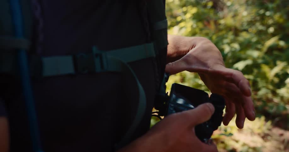 A persons hands hold and look at a digital camera while a backpack hangs from their back