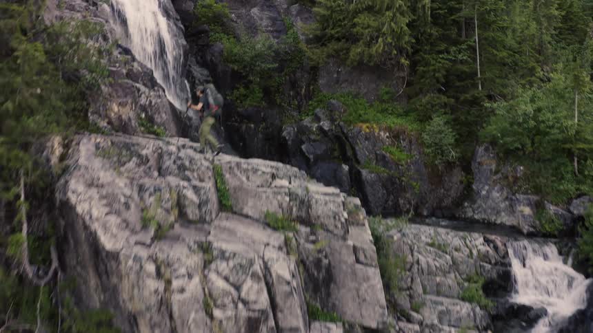 A person walks across a rock face with water flowing down it