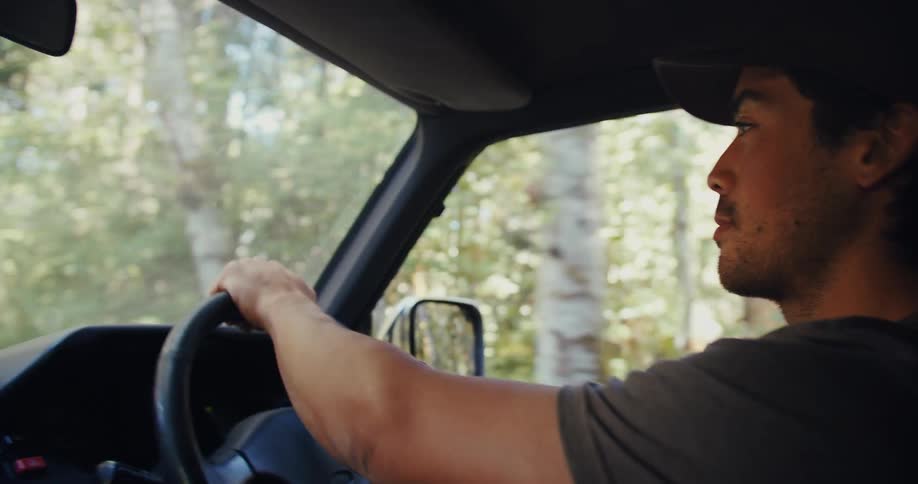 Man driving a car in a rural area at midday along a road lined with trees on both sides