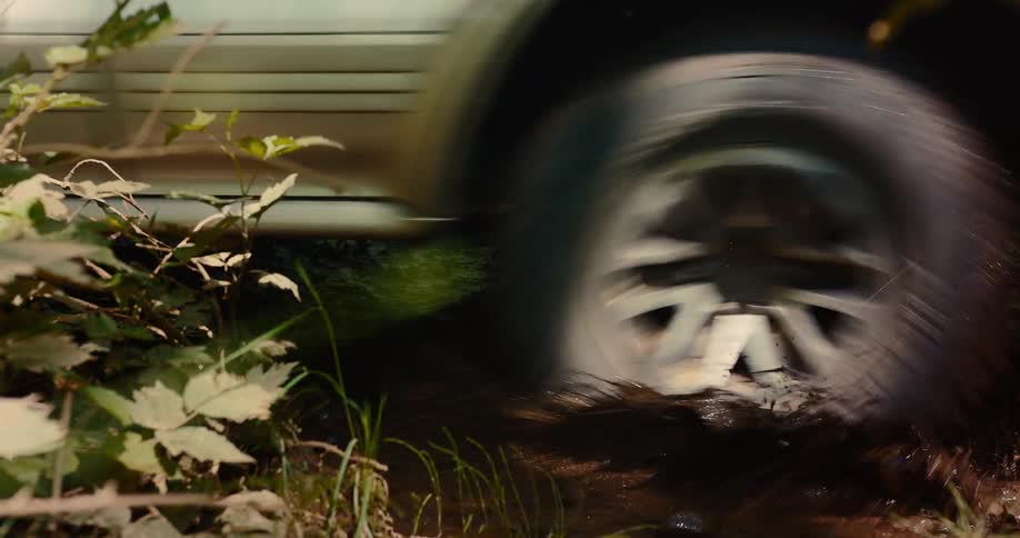 An atv drives over a muddy puddle in a forest splashing out dirty water