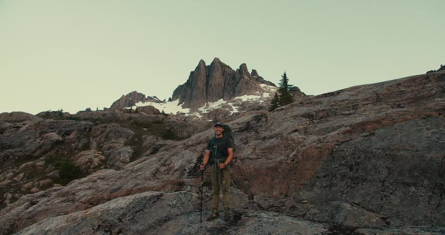Backpacker smiles while standing in mountainous terrain during the daytime
