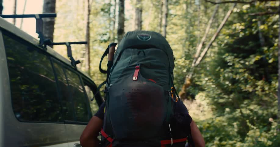 Man with a large backpack walks near a vehicle in the forest