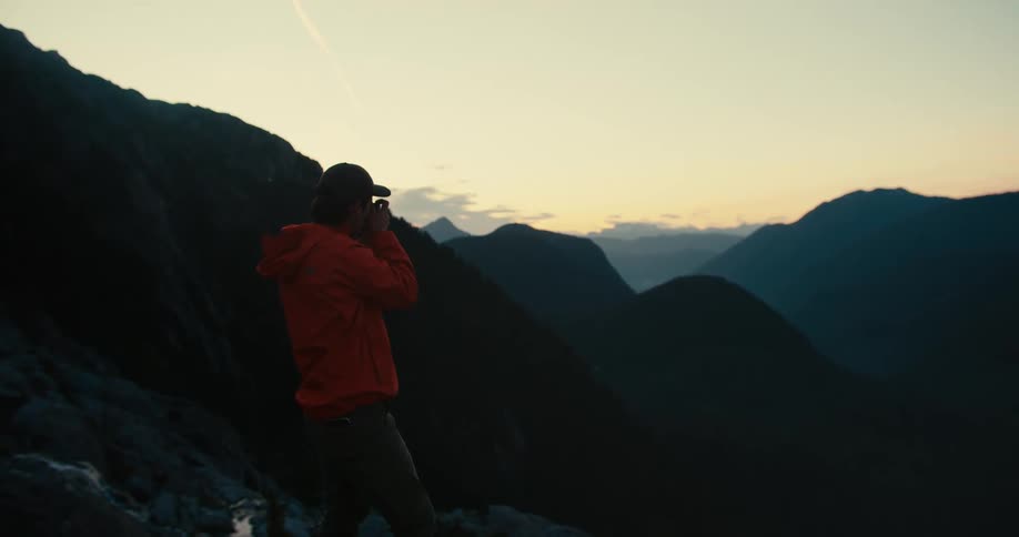 A person in an orange jacket photographs the mountains at sunset