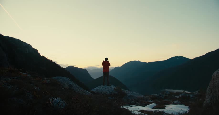 Person standing on a rock overlooks the sunset between mountains