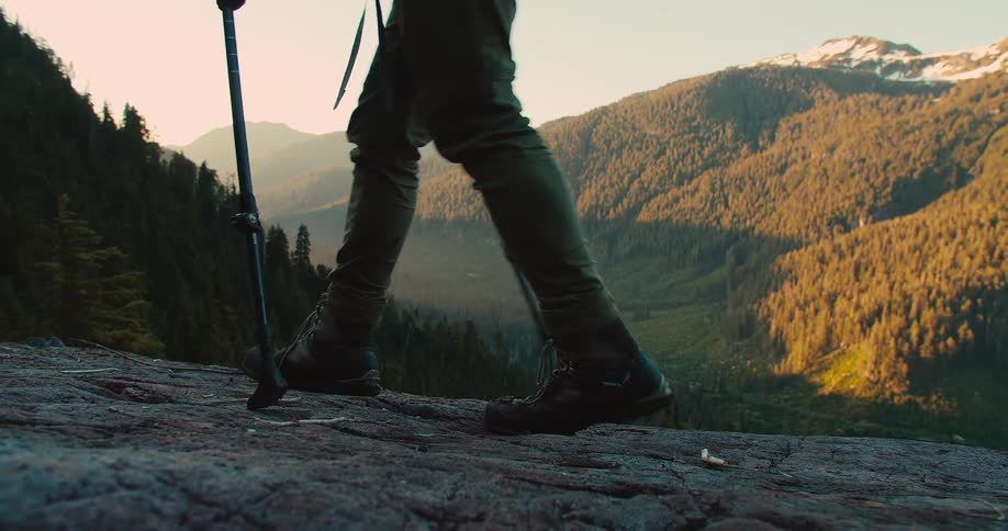 A person hikes with poles on a rocky outcrop at sunset