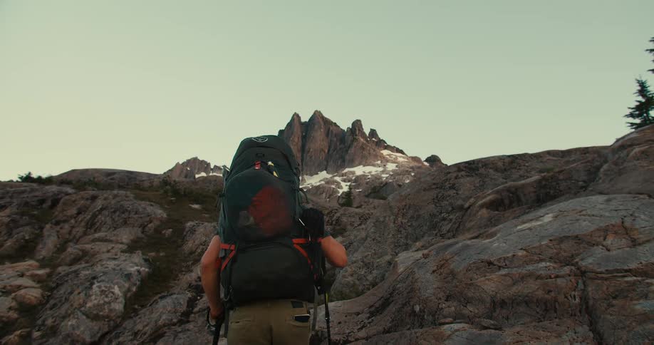 Mountaineer with a large backpack hikes towards a rocky peak