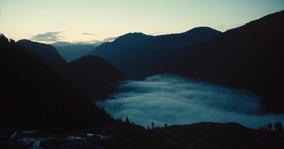 Fog drifts over a lake flowing through mountains at dawn