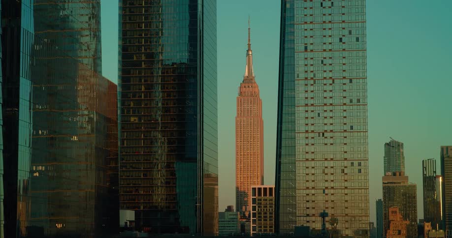 The empire state building glows in the warm light of sunset framed between two tall glass skyscrapers
