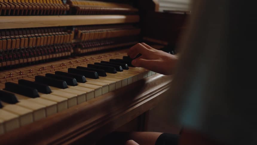 Person playing a grand piano while another person sits beside them watching closely