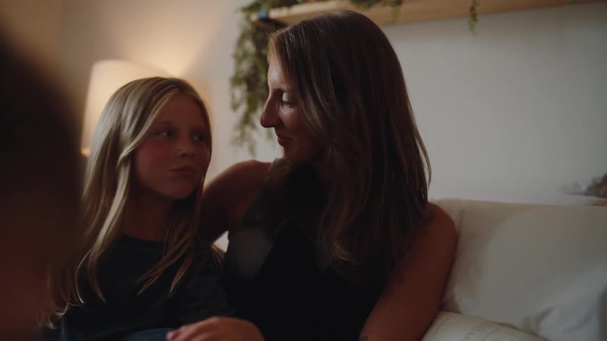 Mother and daughter sitting on the couch leaning their heads against each other in a loving moment