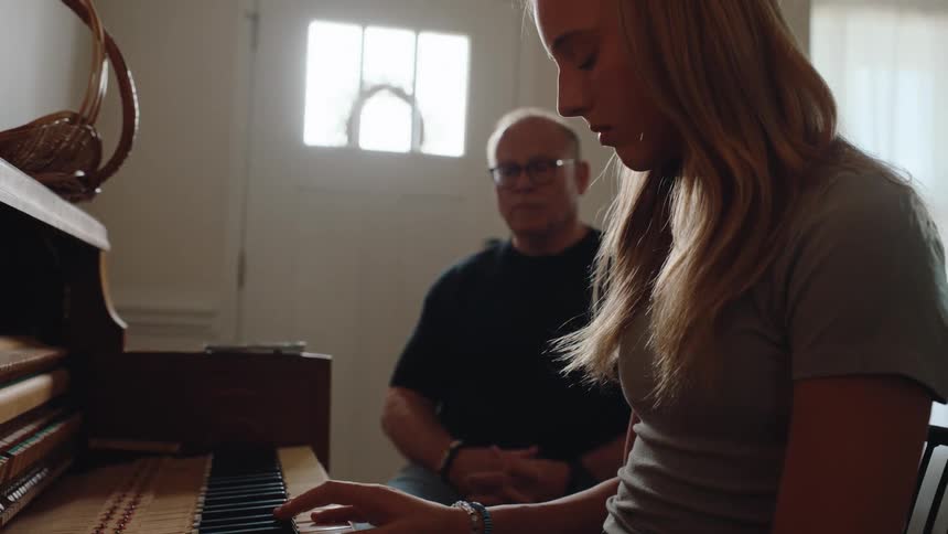 Man with glasses sitting next to a young woman who is playing the piano