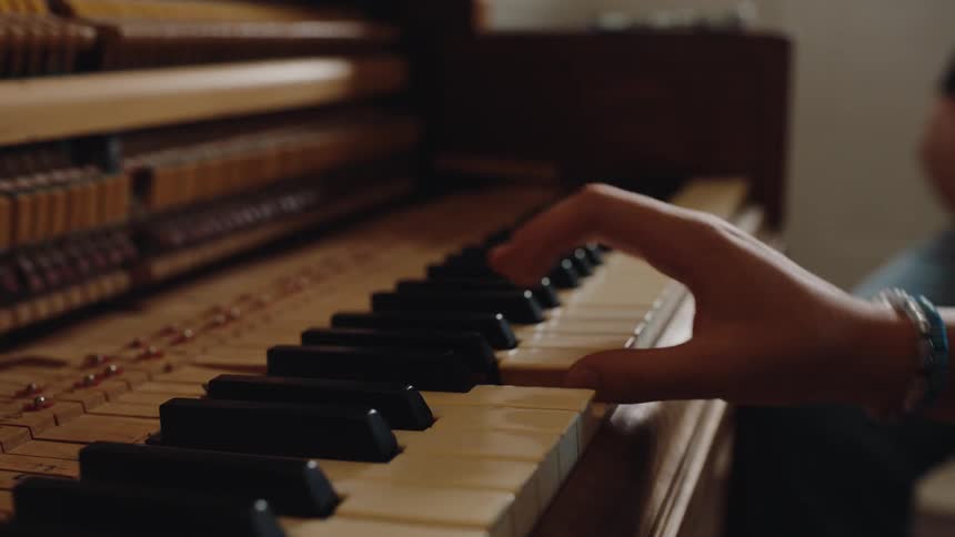 A hand gently presses the keys of an upright piano with its inner workings exposed