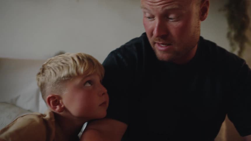 A man with a trimmed beard sits closely with a young blond boy both appearing calm and thoughtful