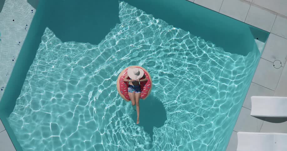 Woman lies on a pool ring float while floating in a swimming pool on a sunny summer day