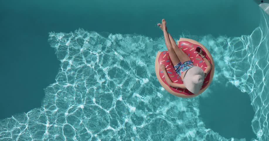 Person relaxes on a donutshaped pool float holding a drink