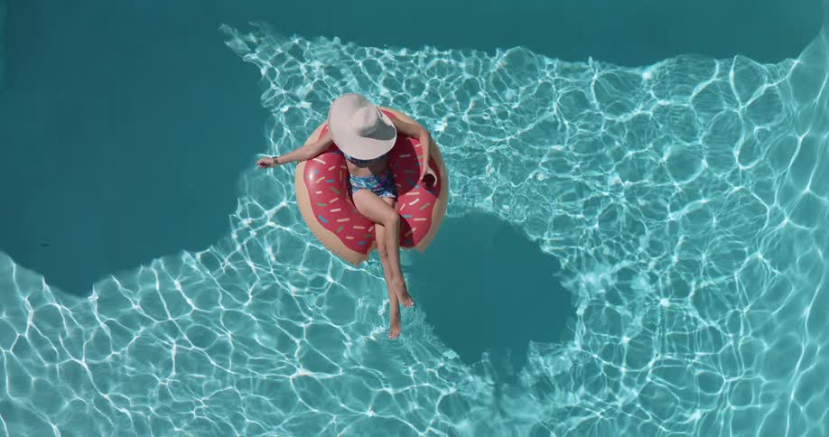 Woman wearing a bikini and a sun hat lies in a ring float in a swimming pool on a summer day