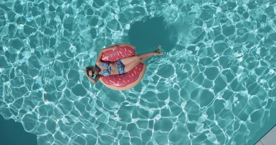 The woman is floating in the middle of the pool on a sunny day