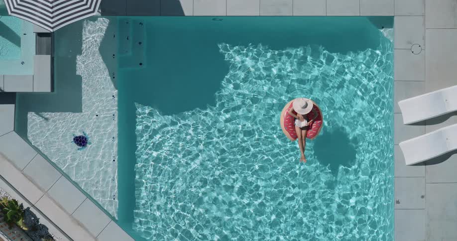 Woman reads while lying on a ring float in a swimming pool on a summer day