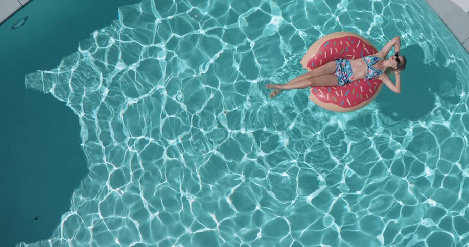 Woman in sunglasses and bikini lying on a float in the pool