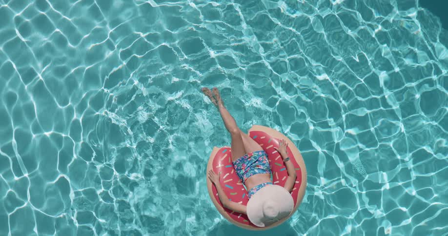 Top view of a woman in a hat lying on a float in the pool
