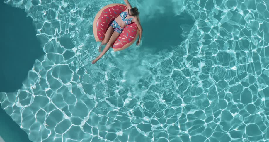 Woman relaxing on a donut float in a crystal blue swimming pool