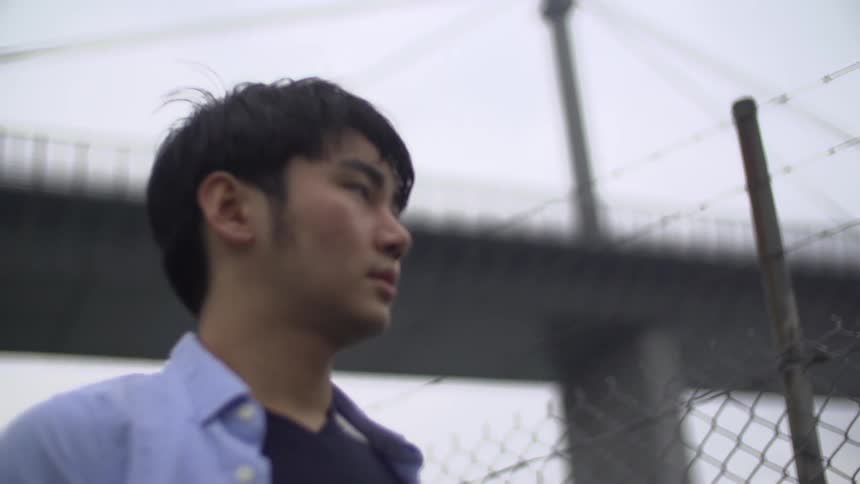 Man walks by a fence with a bridge behind him