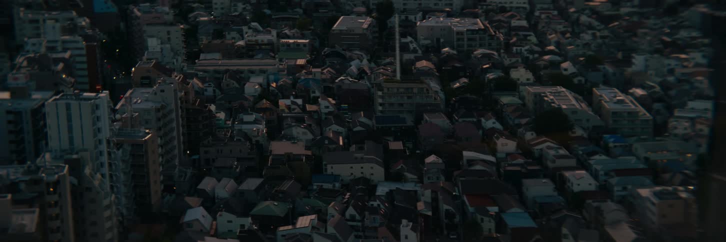 A drone shot captures an expansive view of a densely populated city at dusk the camera slowly pans over the rooftops of countless buildings as the last light of the day fades away